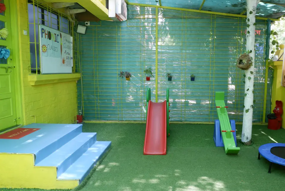 Shaded outdoor play area at Cubs Gurukul with slide, see-saw and trampoline on soft turf